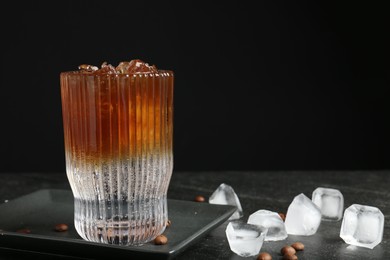 Refreshing espresso tonic drink with ice and coffee beans on dark table, closeup. Space for text