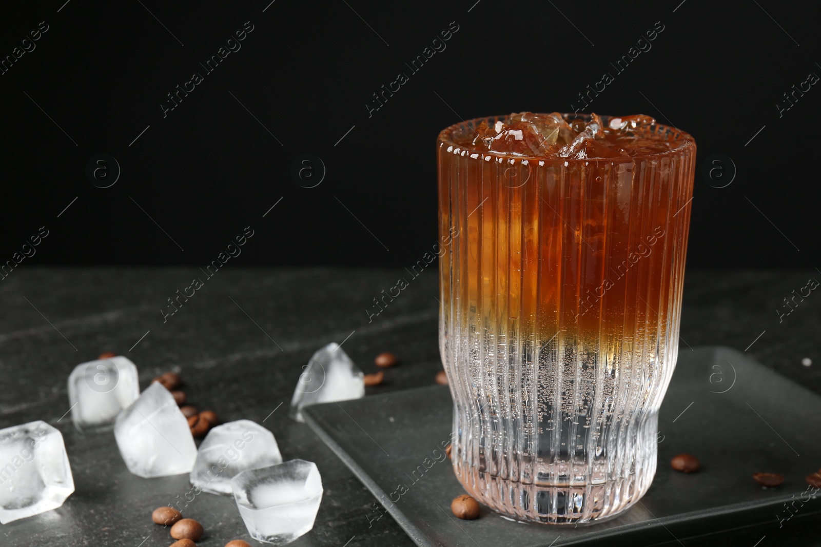 Photo of Refreshing espresso tonic drink with ice and coffee beans on dark table, closeup. Space for text