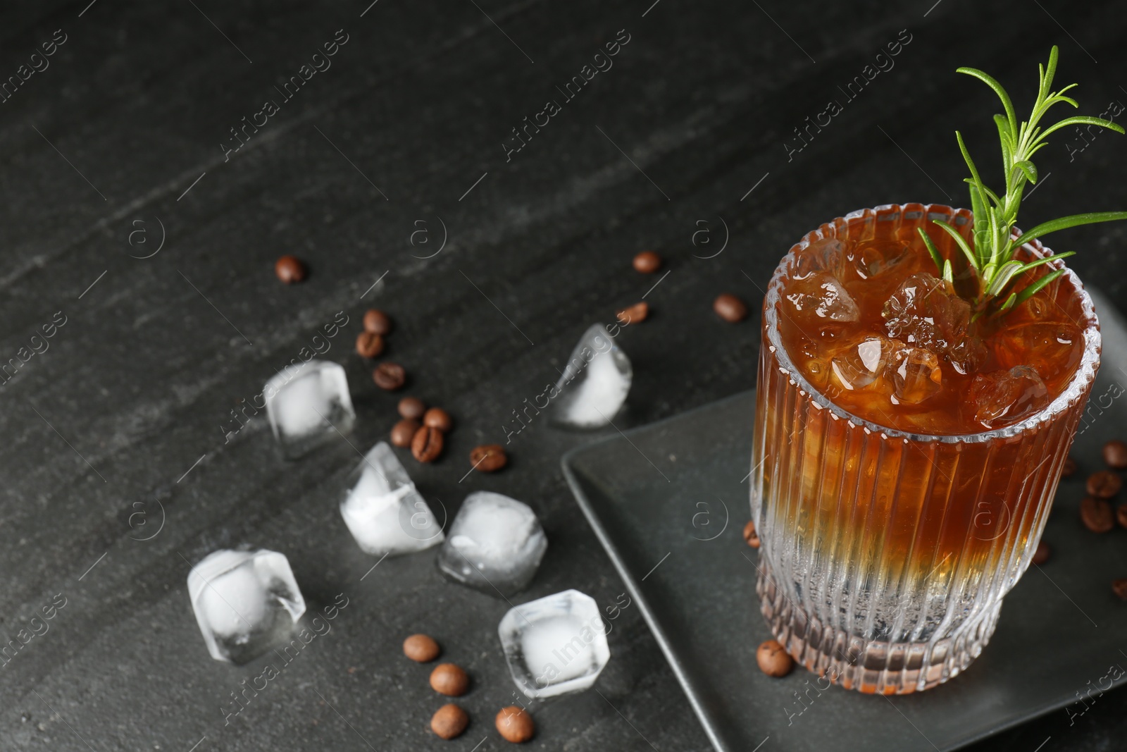 Photo of Refreshing espresso tonic drink with rosemary, ice and coffee beans on dark table, closeup. Space for text