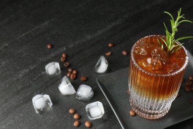 Refreshing espresso tonic drink with rosemary, ice and coffee beans on dark table, closeup. Space for text