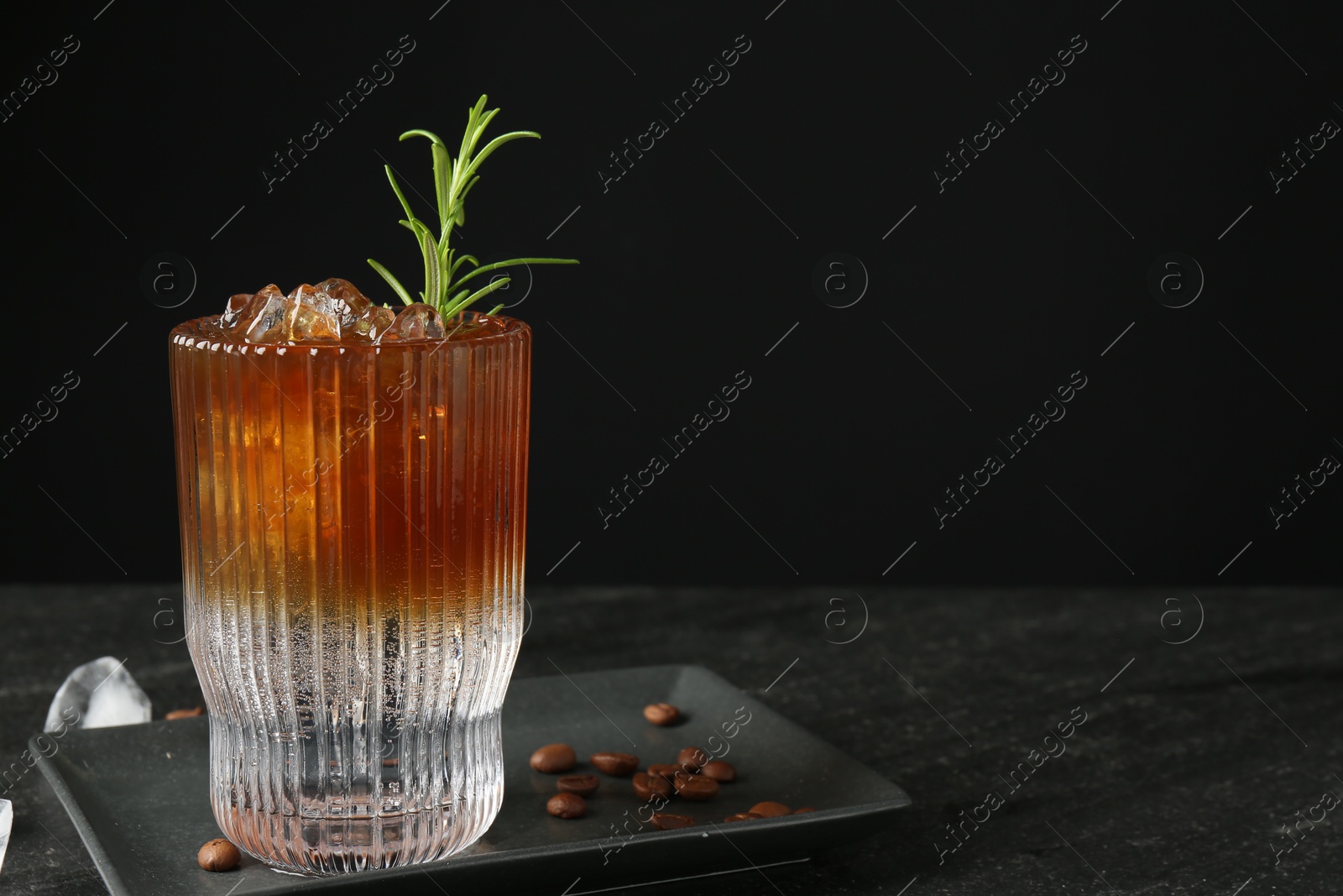 Photo of Refreshing espresso tonic drink with rosemary, ice and coffee beans on dark table. Space for text