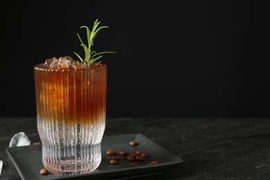 Refreshing espresso tonic drink with rosemary, ice and coffee beans on dark table. Space for text