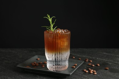 Refreshing espresso tonic drink with rosemary and coffee beans on dark table