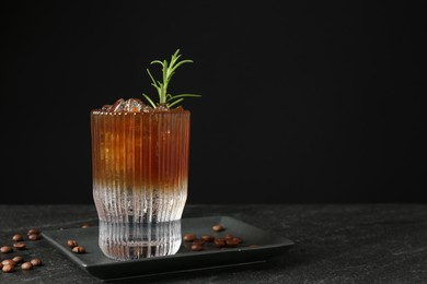 Refreshing espresso tonic drink with rosemary and coffee beans on dark table. Space for text