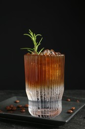 Refreshing espresso tonic drink with rosemary and coffee beans on dark table