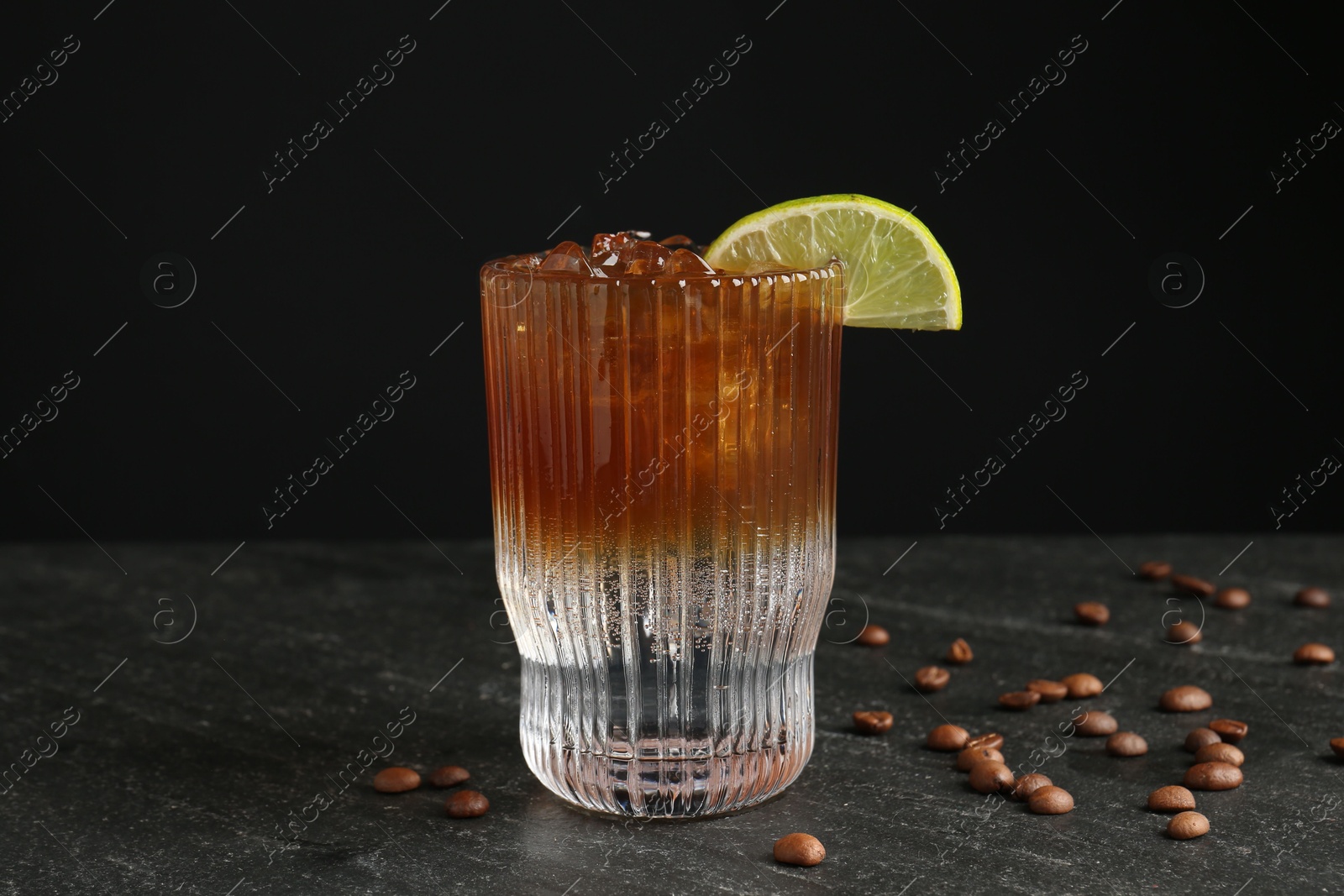 Photo of Refreshing espresso tonic drink with slice of lime and coffee beans on dark table