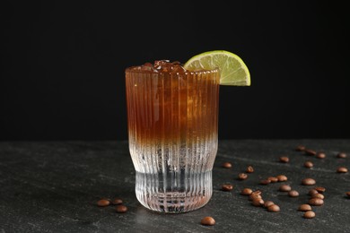 Refreshing espresso tonic drink with slice of lime and coffee beans on dark table