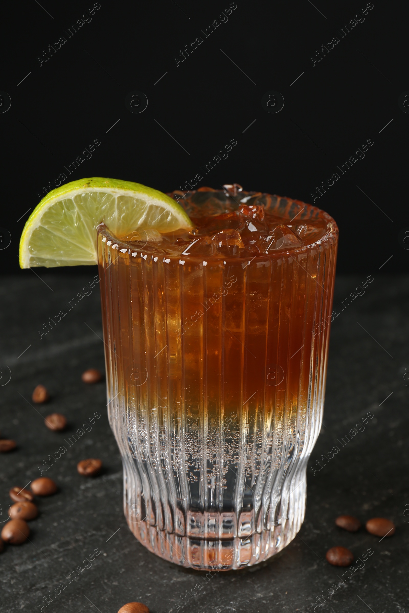 Photo of Refreshing espresso tonic drink with slice of lime and coffee beans on dark table