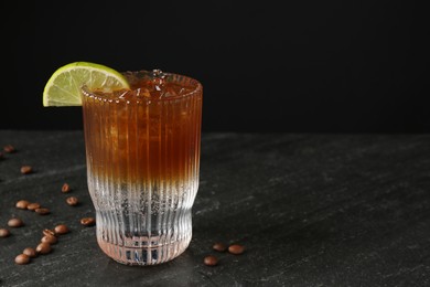 Photo of Refreshing espresso tonic drink with slice of lime and coffee beans on dark table. Space for text