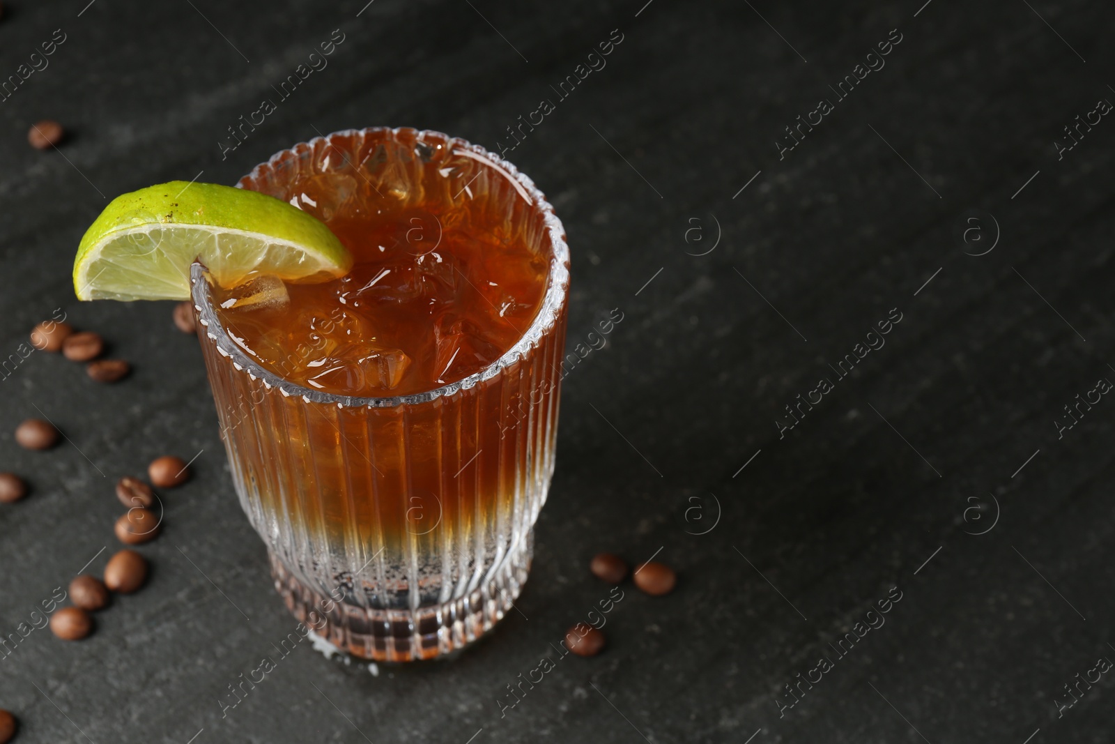 Photo of Refreshing espresso tonic drink with slice of lime and coffee beans on dark table, closeup. Space for text