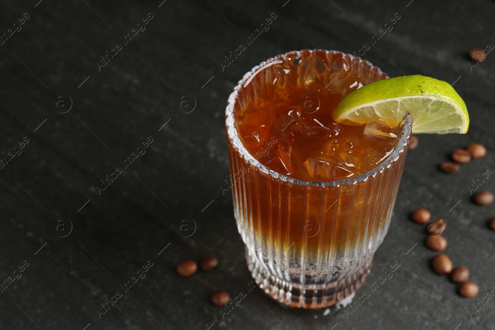 Photo of Refreshing espresso tonic drink with slice of lime and coffee beans on dark table, closeup. Space for text