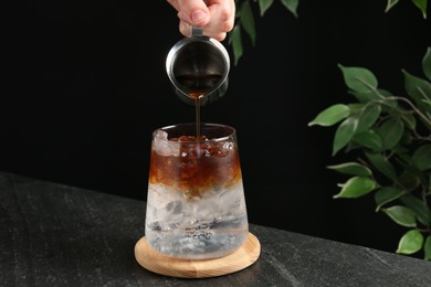 Photo of Woman making refreshing espresso tonic drink at dark table, closeup