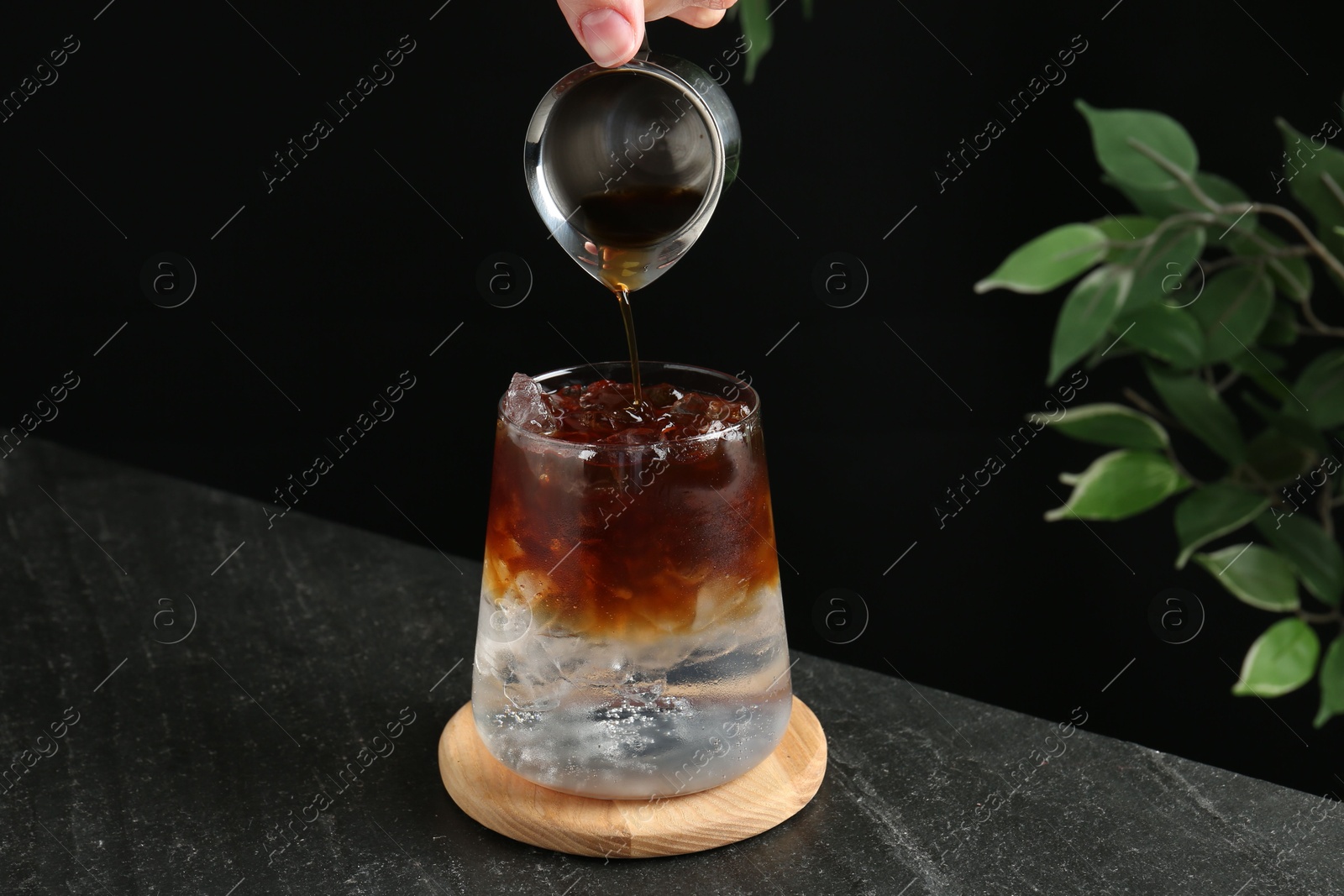 Photo of Woman making refreshing espresso tonic drink at dark table, closeup