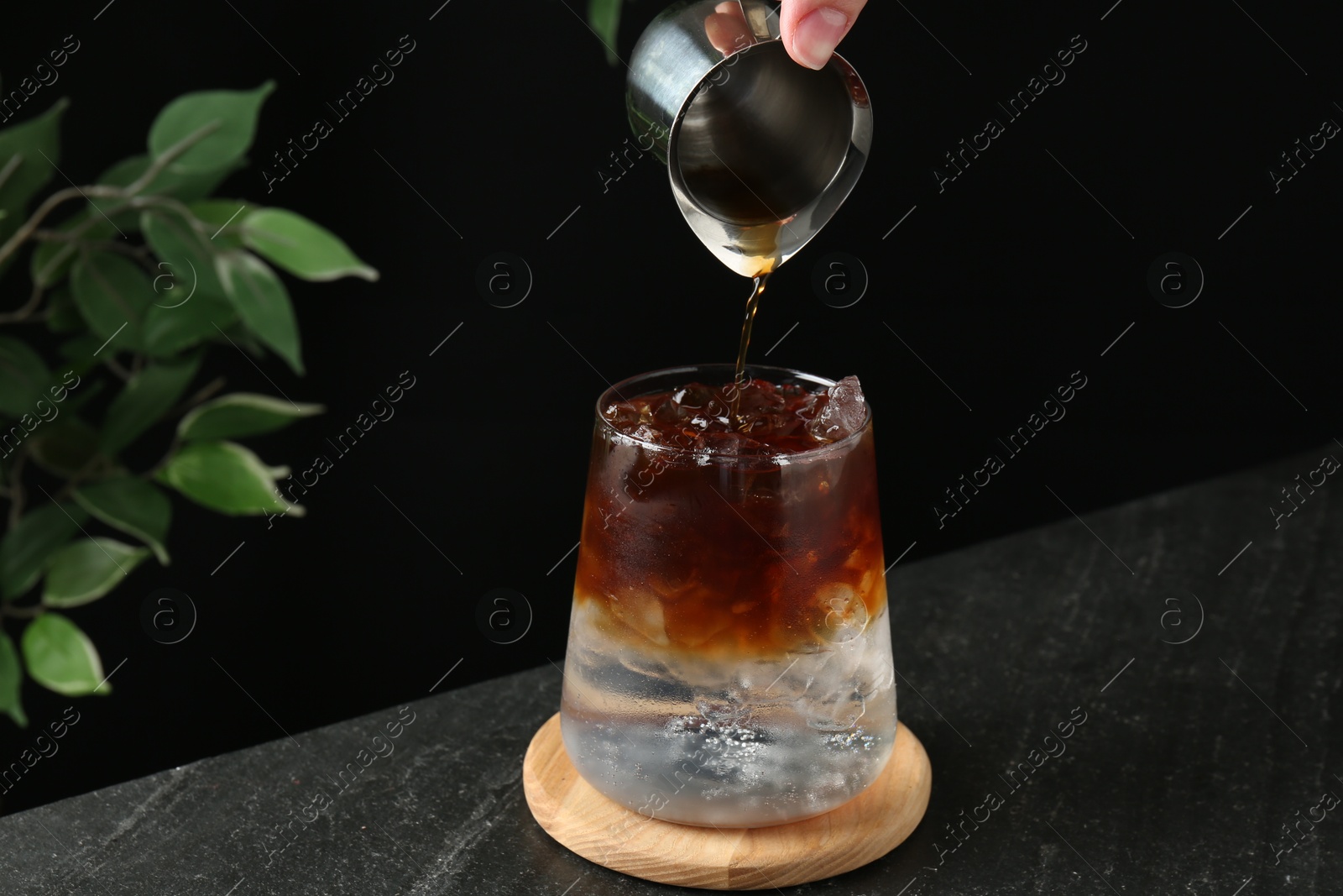 Photo of Woman making refreshing espresso tonic drink at dark table, closeup