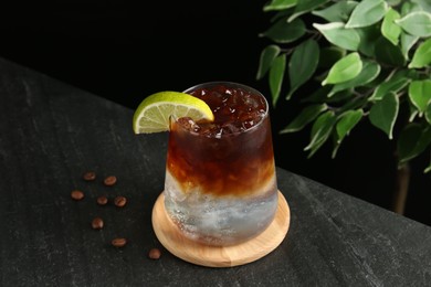 Photo of Refreshing espresso tonic drink with slice of lime and coffee beans on dark table