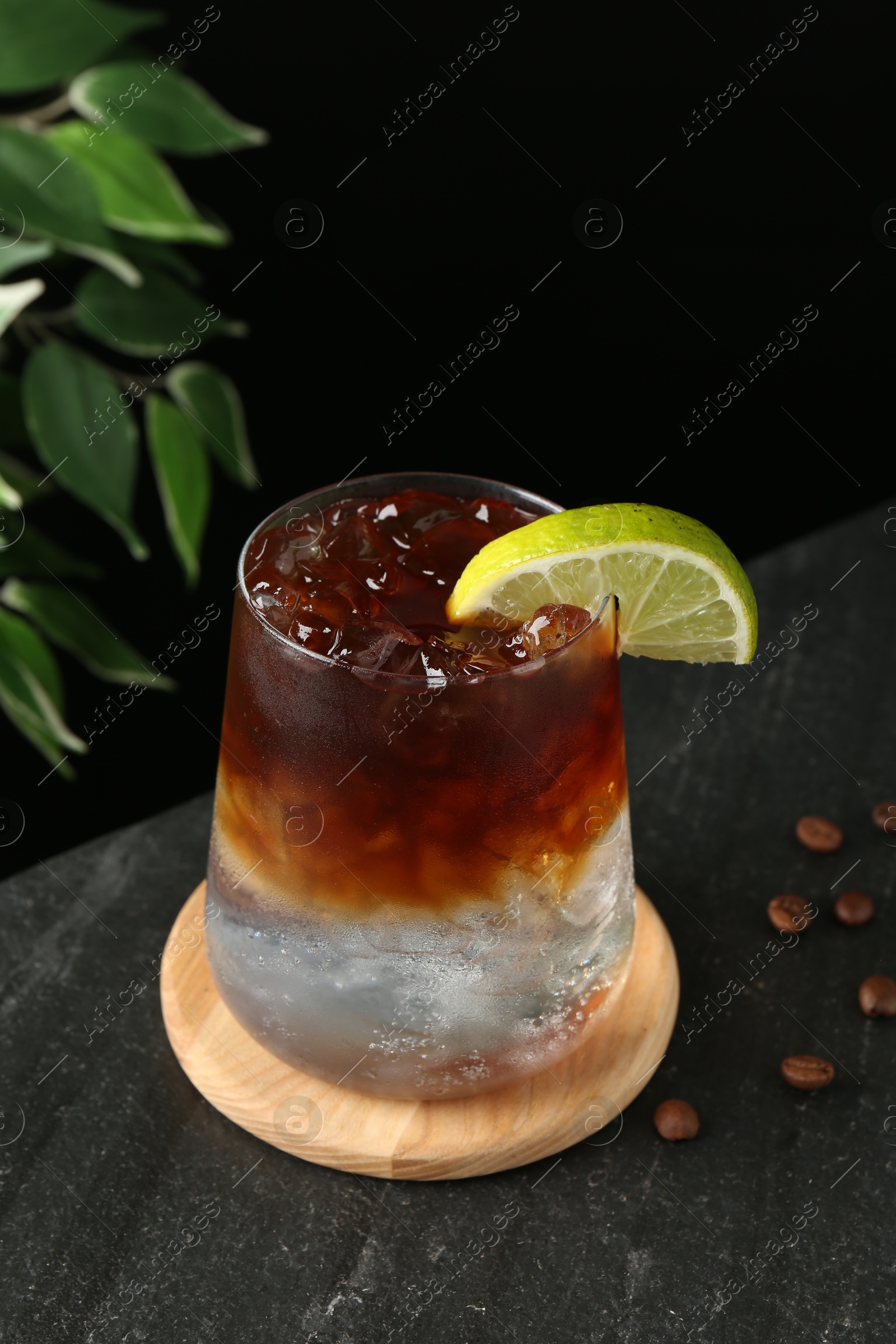 Photo of Refreshing espresso tonic drink with slice of lime and coffee beans on dark table