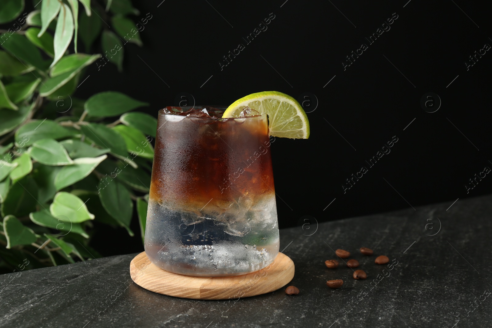 Photo of Refreshing espresso tonic drink with slice of lime and coffee beans on dark table