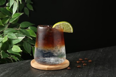 Refreshing espresso tonic drink with slice of lime and coffee beans on dark table