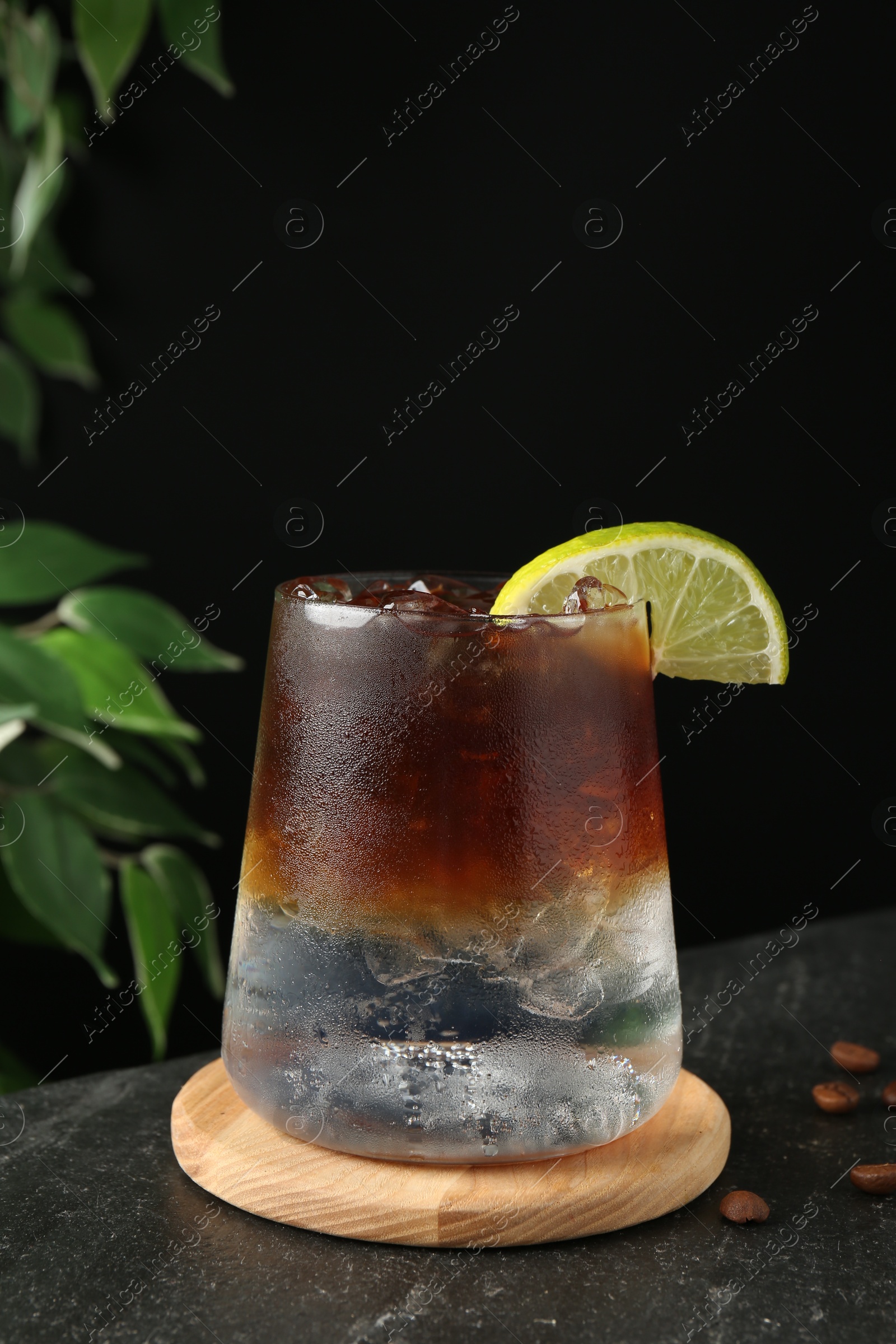 Photo of Refreshing espresso tonic drink with slice of lime and coffee beans on dark table