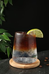 Refreshing espresso tonic drink with slice of lime and coffee beans on dark table