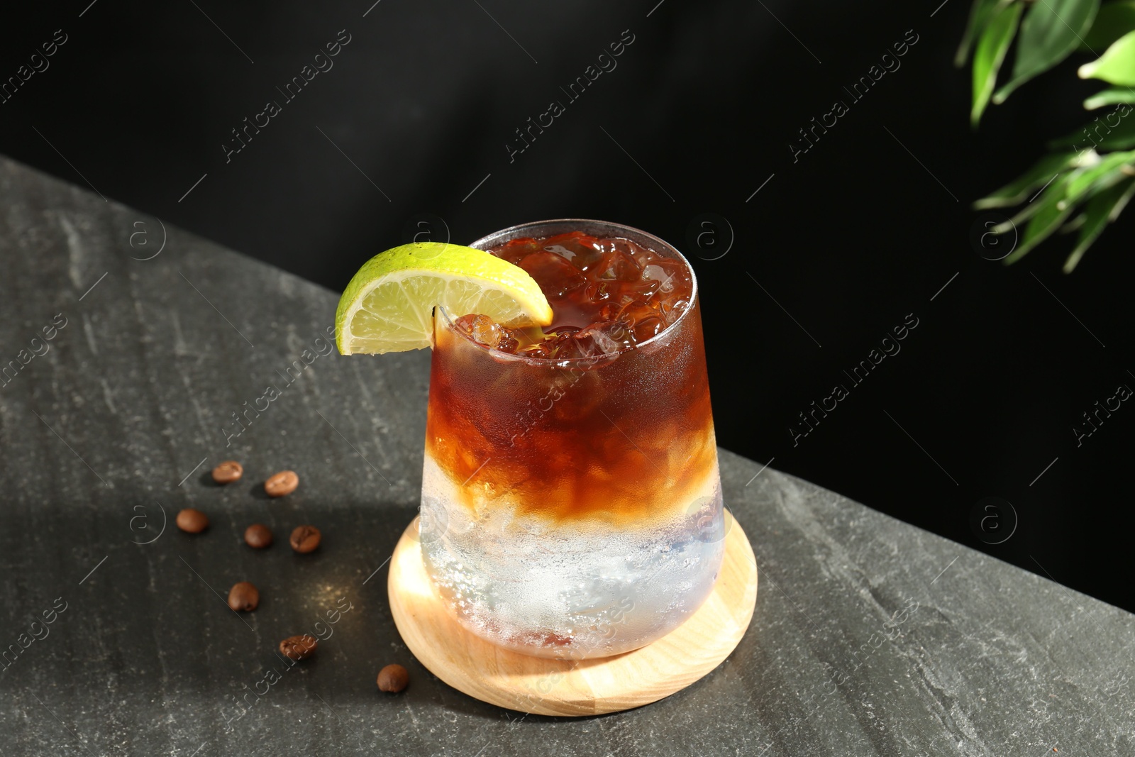 Photo of Refreshing espresso tonic drink with slice of lime and coffee beans on dark table