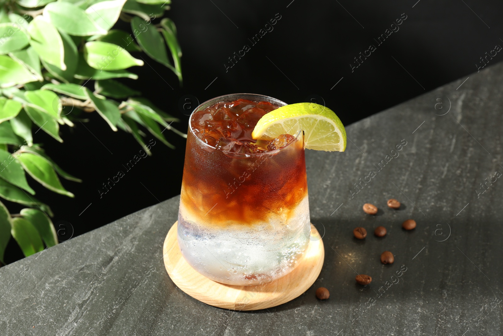 Photo of Refreshing espresso tonic drink with slice of lime and coffee beans on dark table