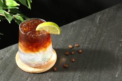 Photo of Refreshing espresso tonic drink with slice of lime and coffee beans on dark table, closeup. Space for text