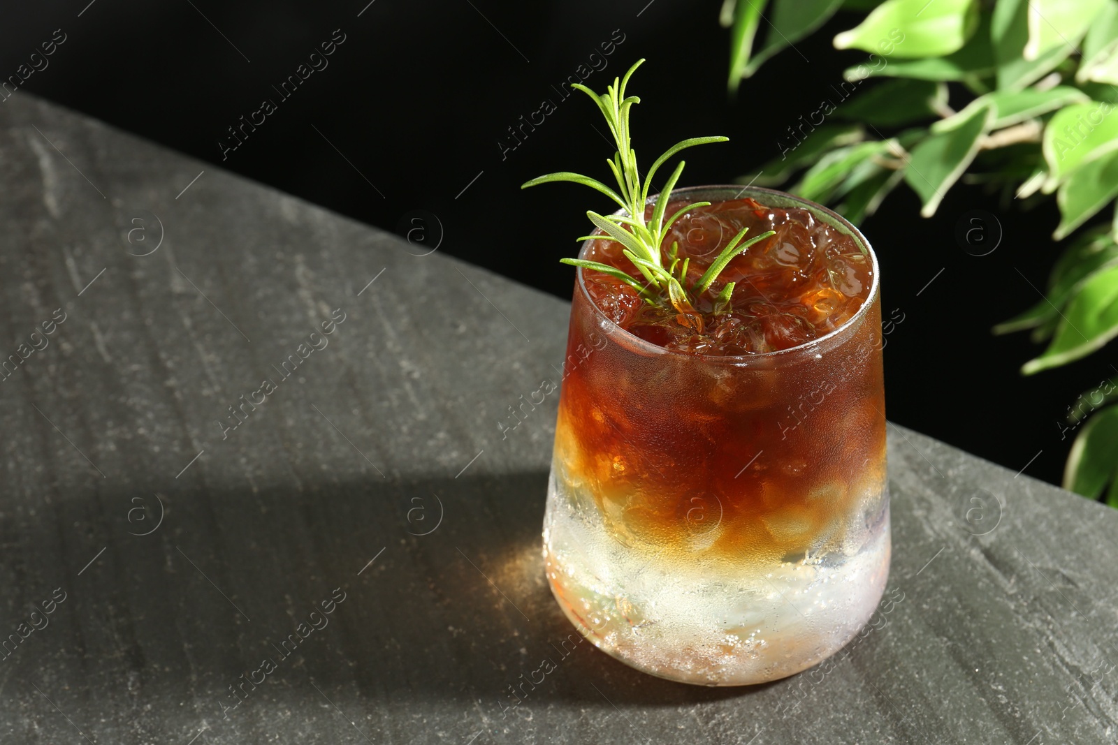 Photo of Refreshing espresso tonic drink with rosemary on dark table, closeup. Space for text