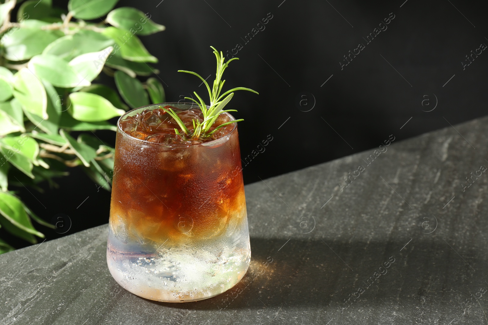 Photo of Refreshing espresso tonic drink with rosemary on dark table. Space for text