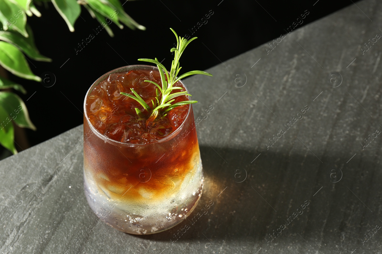 Photo of Refreshing espresso tonic drink with rosemary on dark table, closeup. Space for text