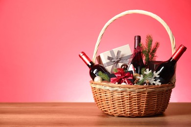 Photo of Wicker gift basket with wine on wooden table against pink background, space for text