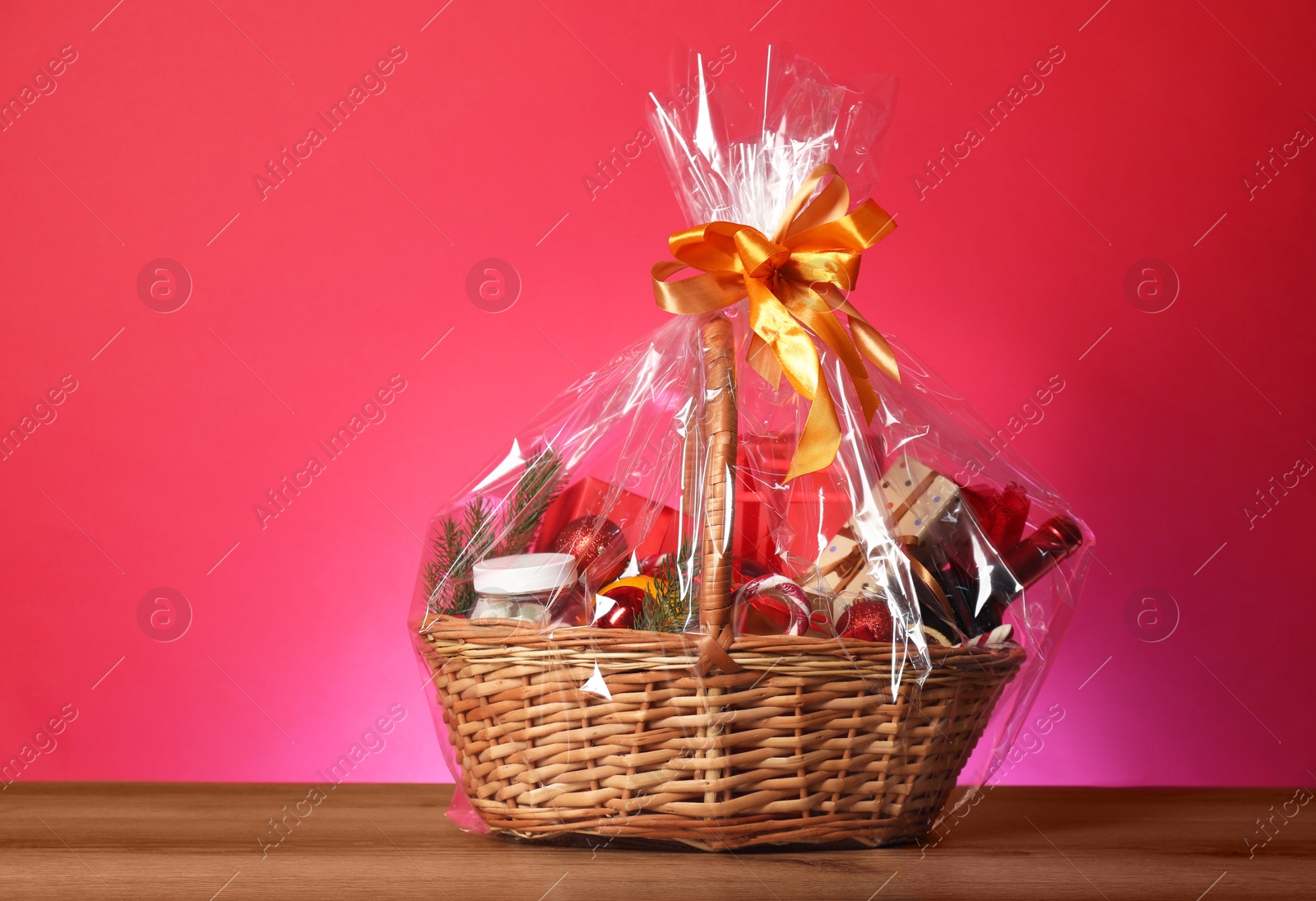 Photo of Wicker gift basket with wine on wooden table against pink background