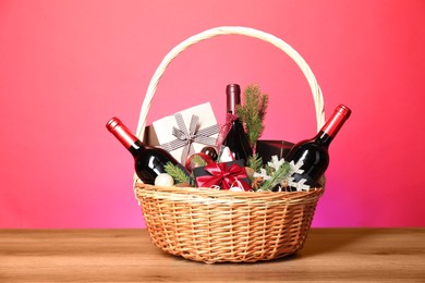 Photo of Wicker gift basket with wine on wooden table against pink background