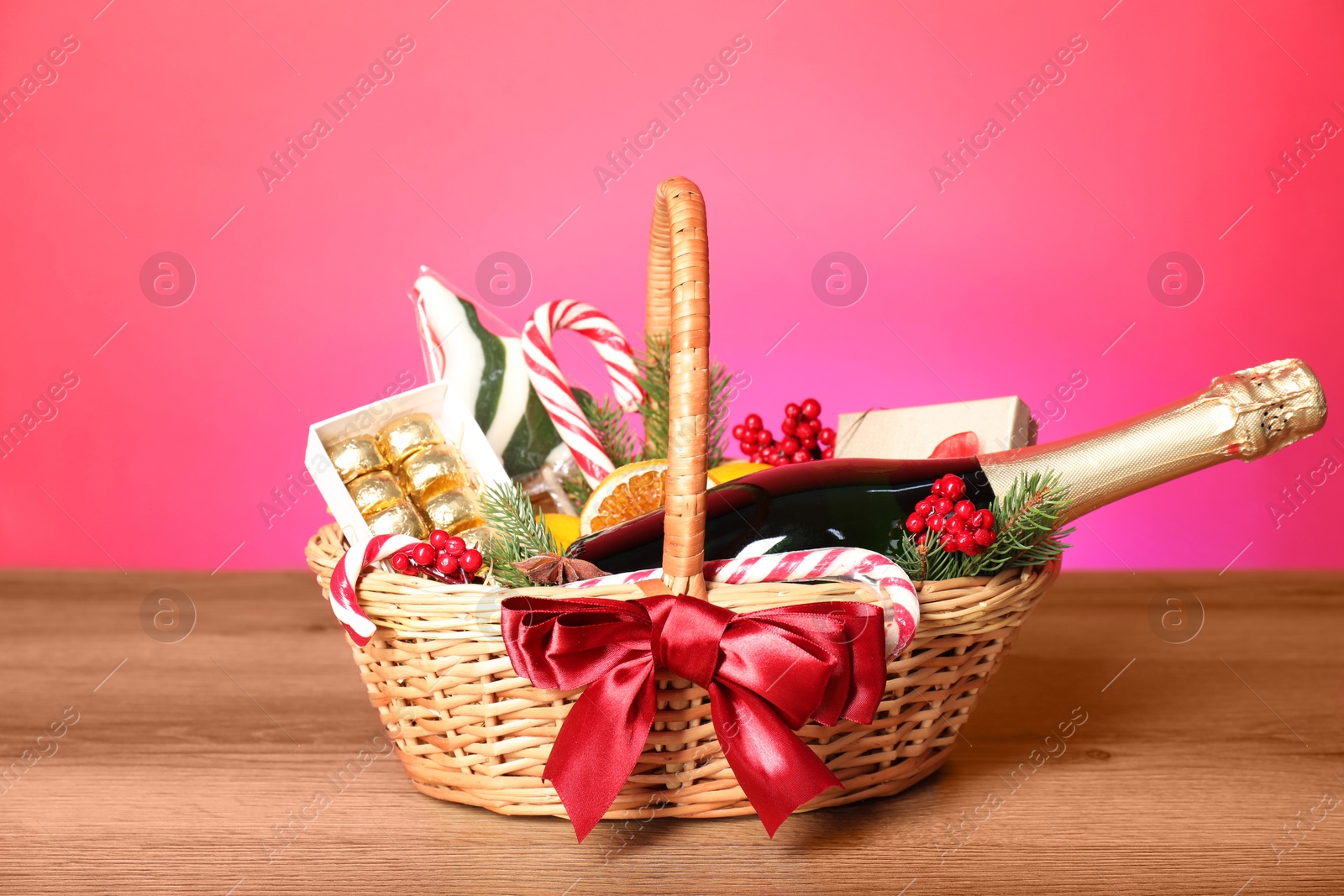 Photo of Wicker gift basket with wine on wooden table against pink background