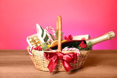 Wicker gift basket with wine on wooden table against pink background