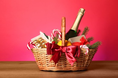 Photo of Wicker gift basket with wine on wooden table against pink background