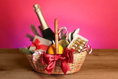 Wicker gift basket with wine on wooden table against pink background