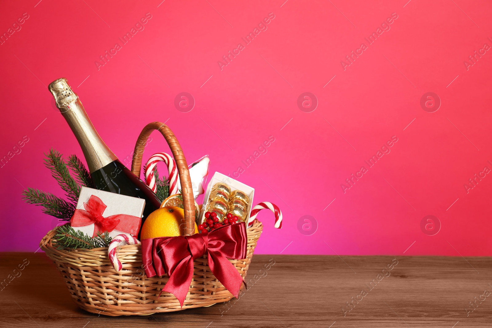 Photo of Wicker gift basket with wine on wooden table against pink background, space for text