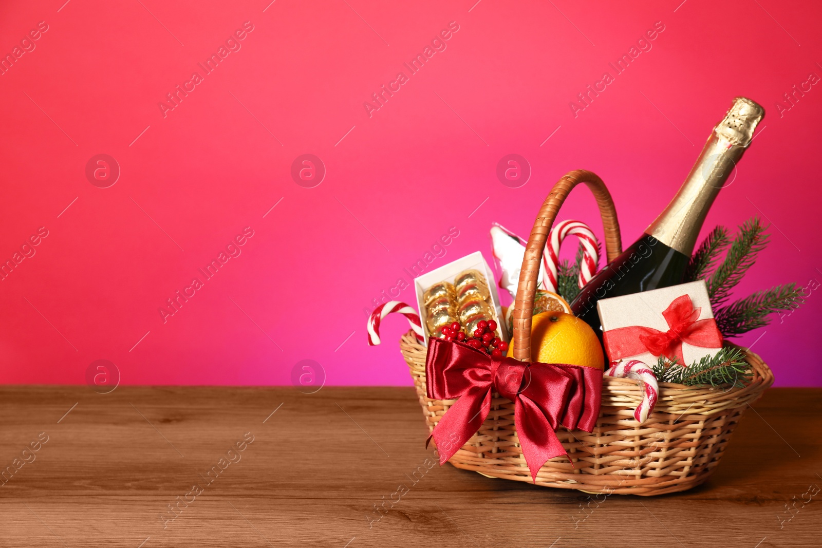 Photo of Wicker gift basket with wine on wooden table against pink background, space for text