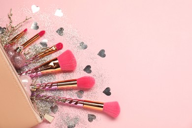 Photo of Cosmetic bag with makeup brushes and Christmas decor on pink background, top view. Space for text