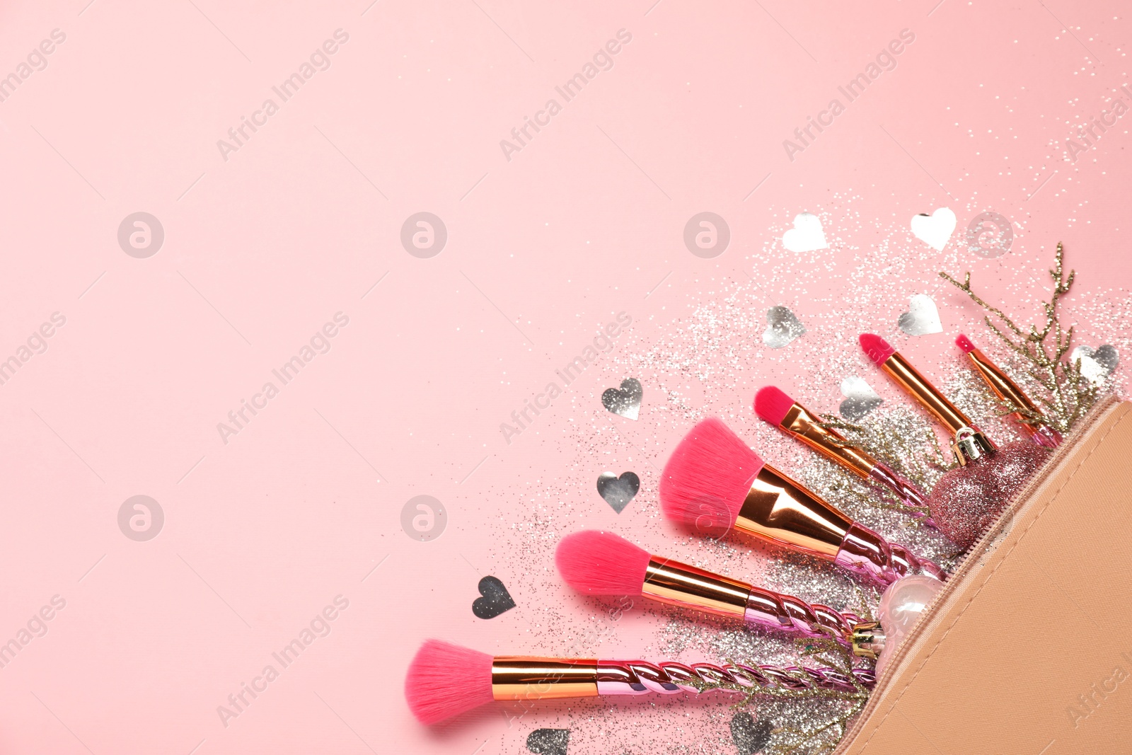 Photo of Cosmetic bag with makeup brushes and Christmas decor on pink background, top view. Space for text