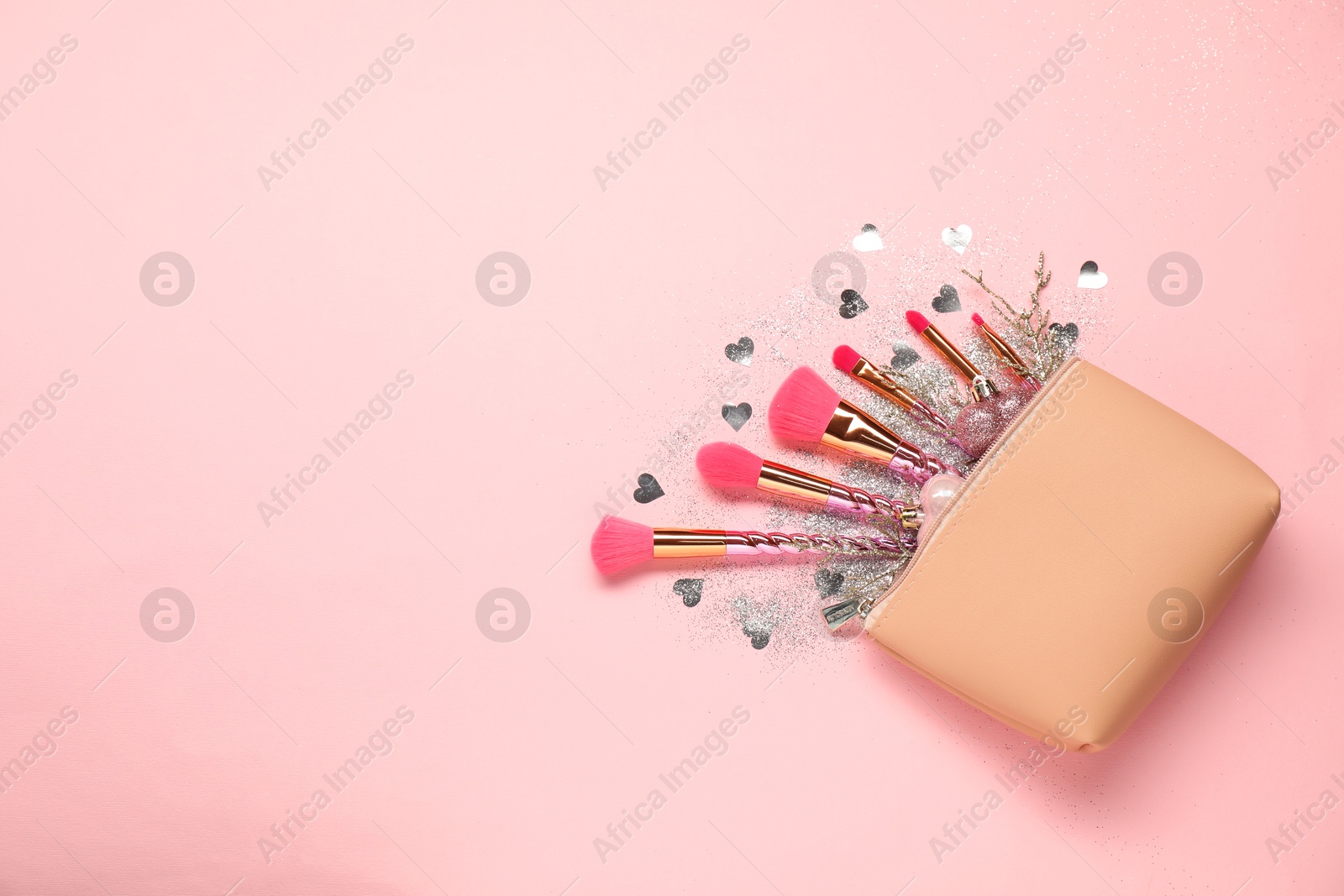 Photo of Cosmetic bag with makeup brushes and Christmas decor on pink background, top view. Space for text