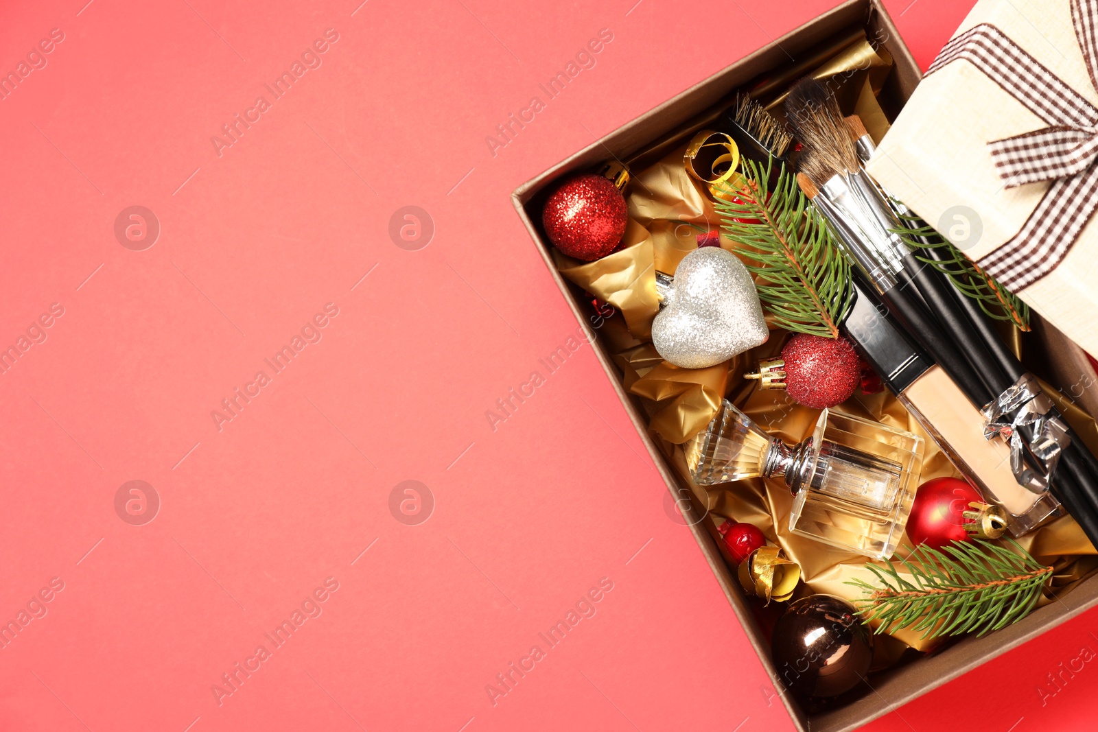 Photo of Makeup brushes, cosmetic product, perfume and Christmas decor in box on coral background, top view. Space for text