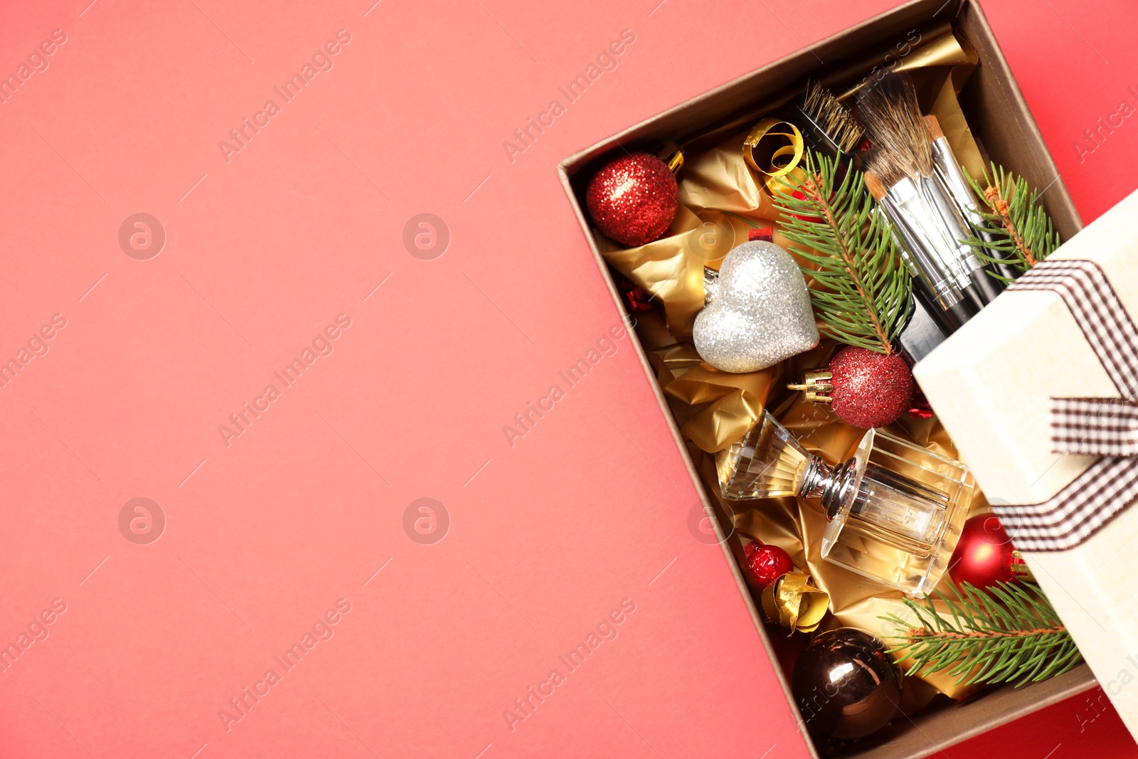 Photo of Makeup brushes, cosmetic product, perfume and Christmas decor in box on coral background, top view. Space for text