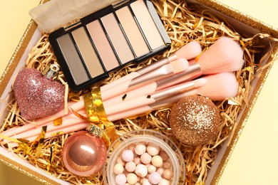 Photo of Makeup brushes, blush and Christmas decor in box on yellow background, top view