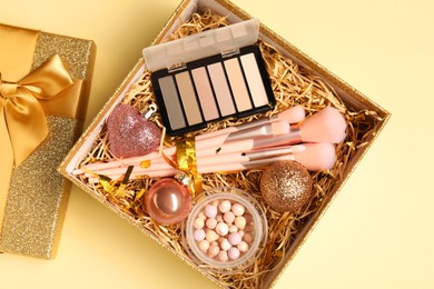 Photo of Makeup brushes, blush and Christmas decor in box on yellow background, top view