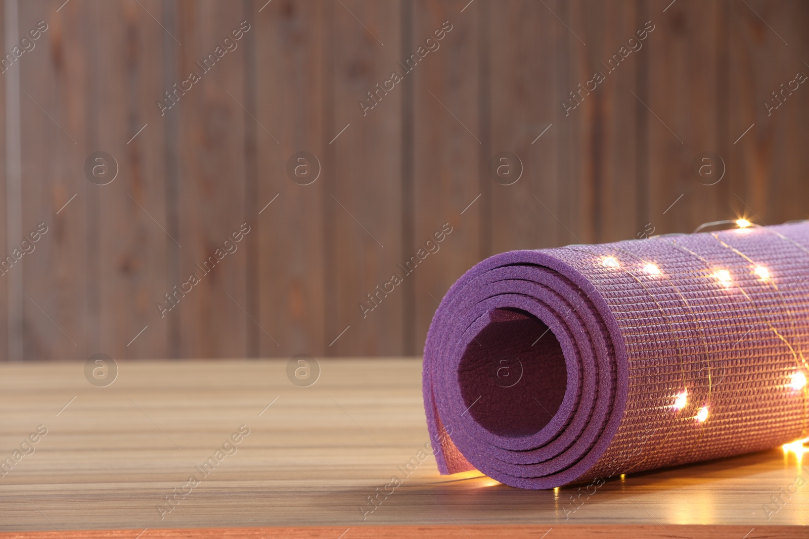 Photo of Yoga mat with Christmas lights on wooden surface. Space for text