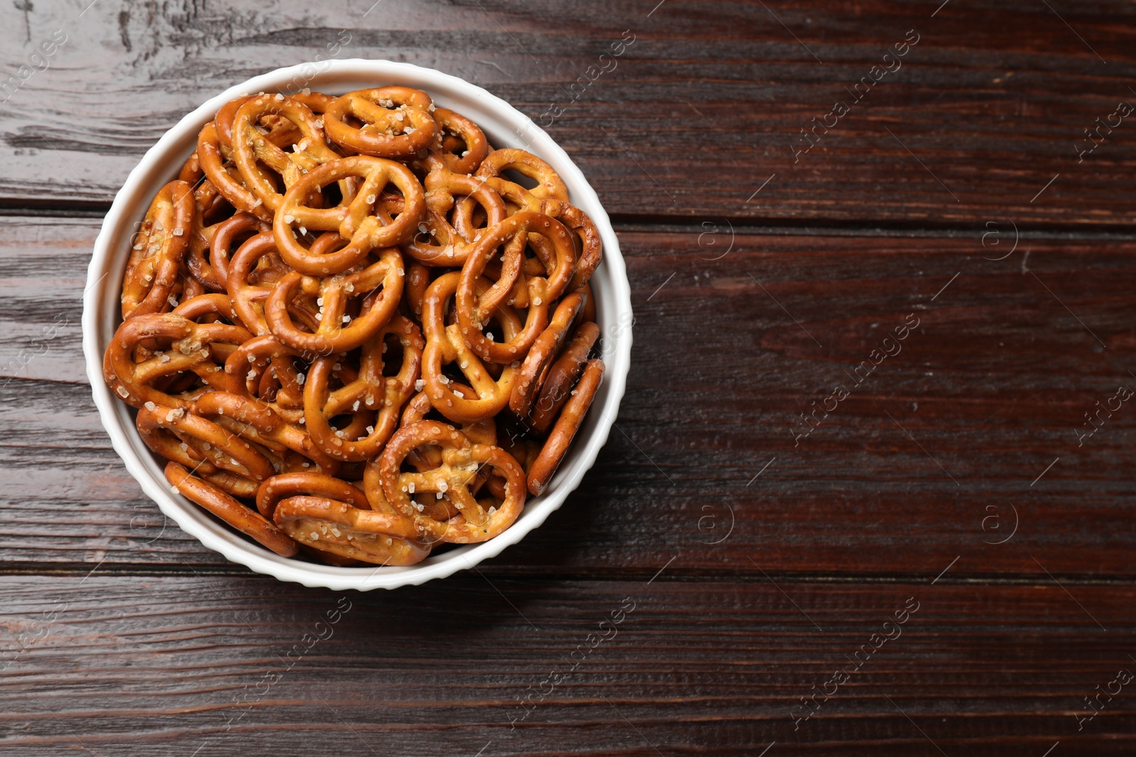 Photo of Tasty pretzel crackers in bowl on wooden table, top view. Space for text