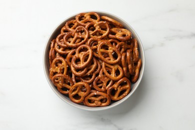 Photo of Tasty pretzel crackers in bowl on white marble table, top view