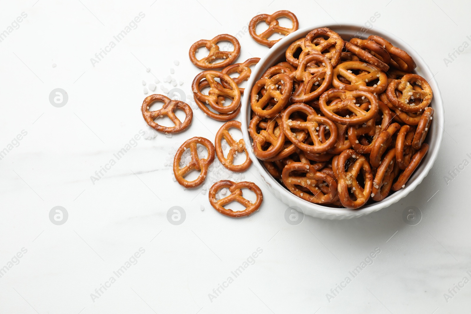 Photo of Tasty pretzel crackers with salt on white marble table, top view. Space for text